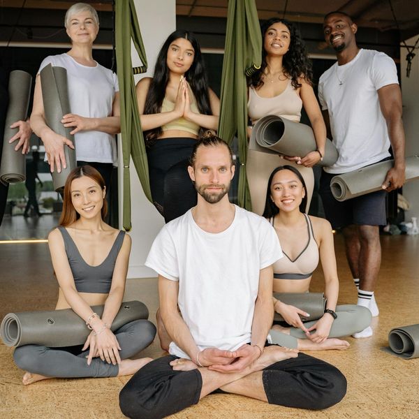 A diverse group of people smiling and preparing for a yoga class.